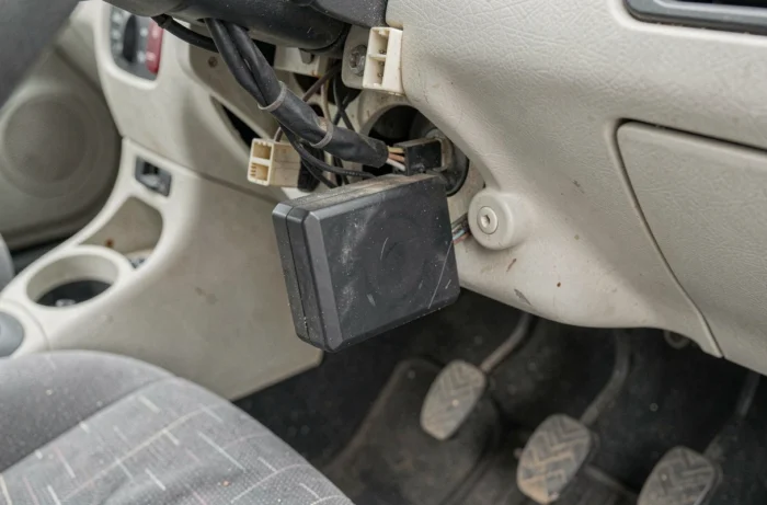 Gros plan sur le boîtier anti démarrage d'une Clio 2 fixé sous le tableau de bord avec les connecteurs et faisceaux de câbles visibles